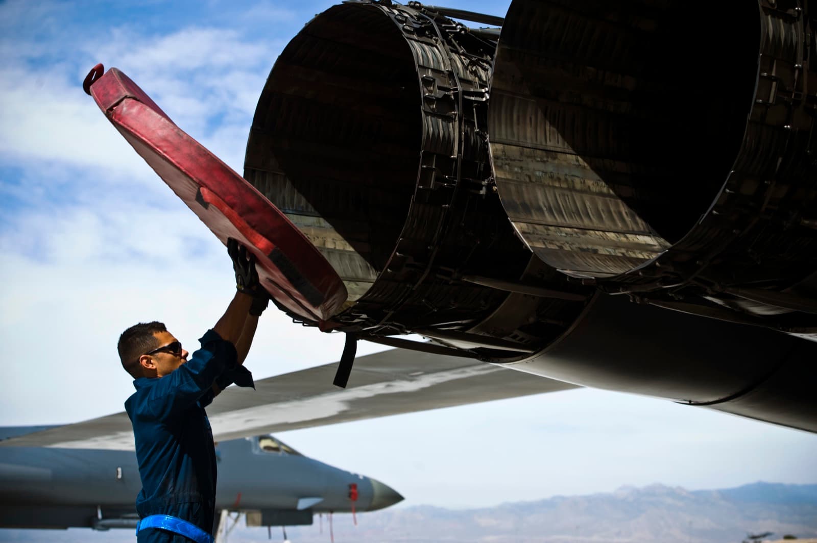 A crew chief lowering an engine access panel on the flight line