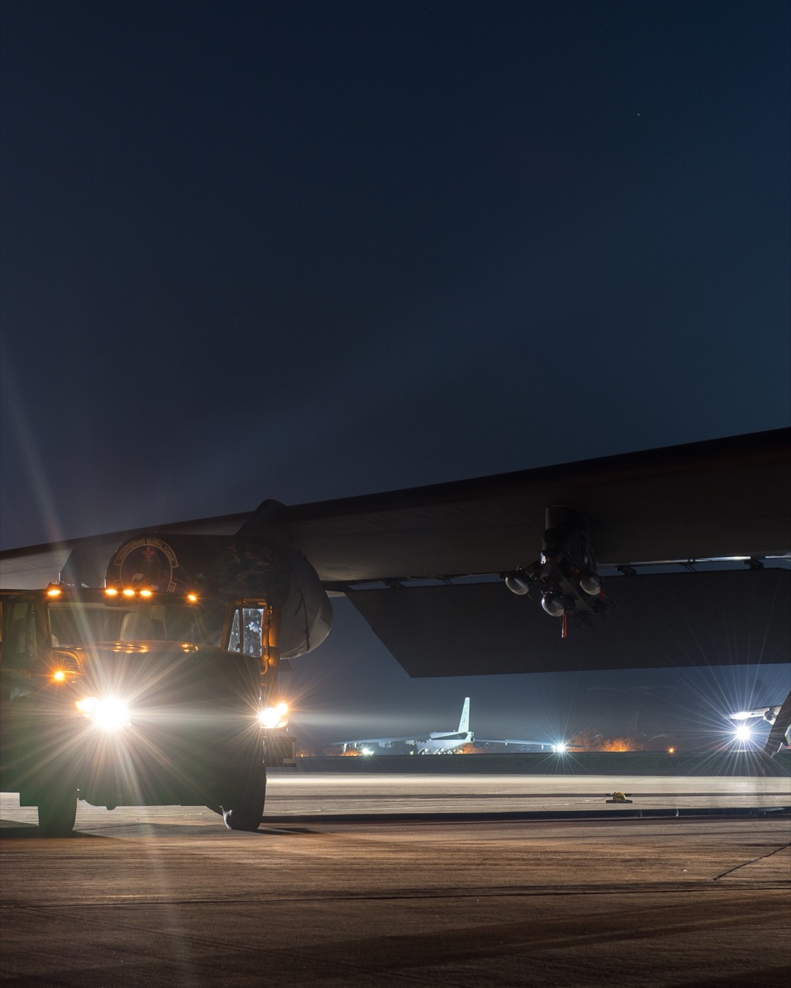 Maintenance crew and support vehicles working under a bomber on the flight line at night
